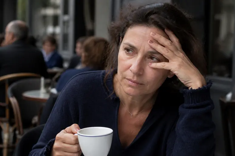 Une femme française d'âge moyen montre des signes de stress, son paupière tremblant légèrement au milieu d'une journée chargée.