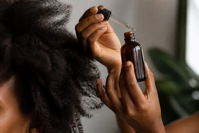 Flacon d'huile végétale et chevelure créépue pour illustrer les soins capillaires adaptés