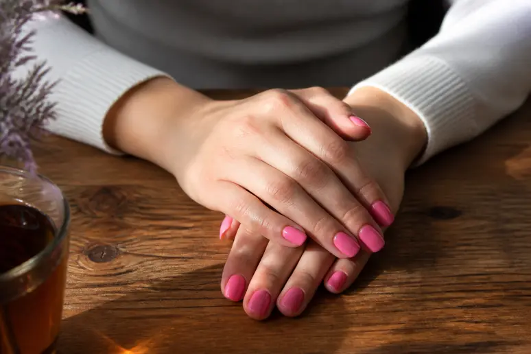 Mains présentant une manucure soignée avec une couleur ongle rose fluo brillante et parfaitement séchée.